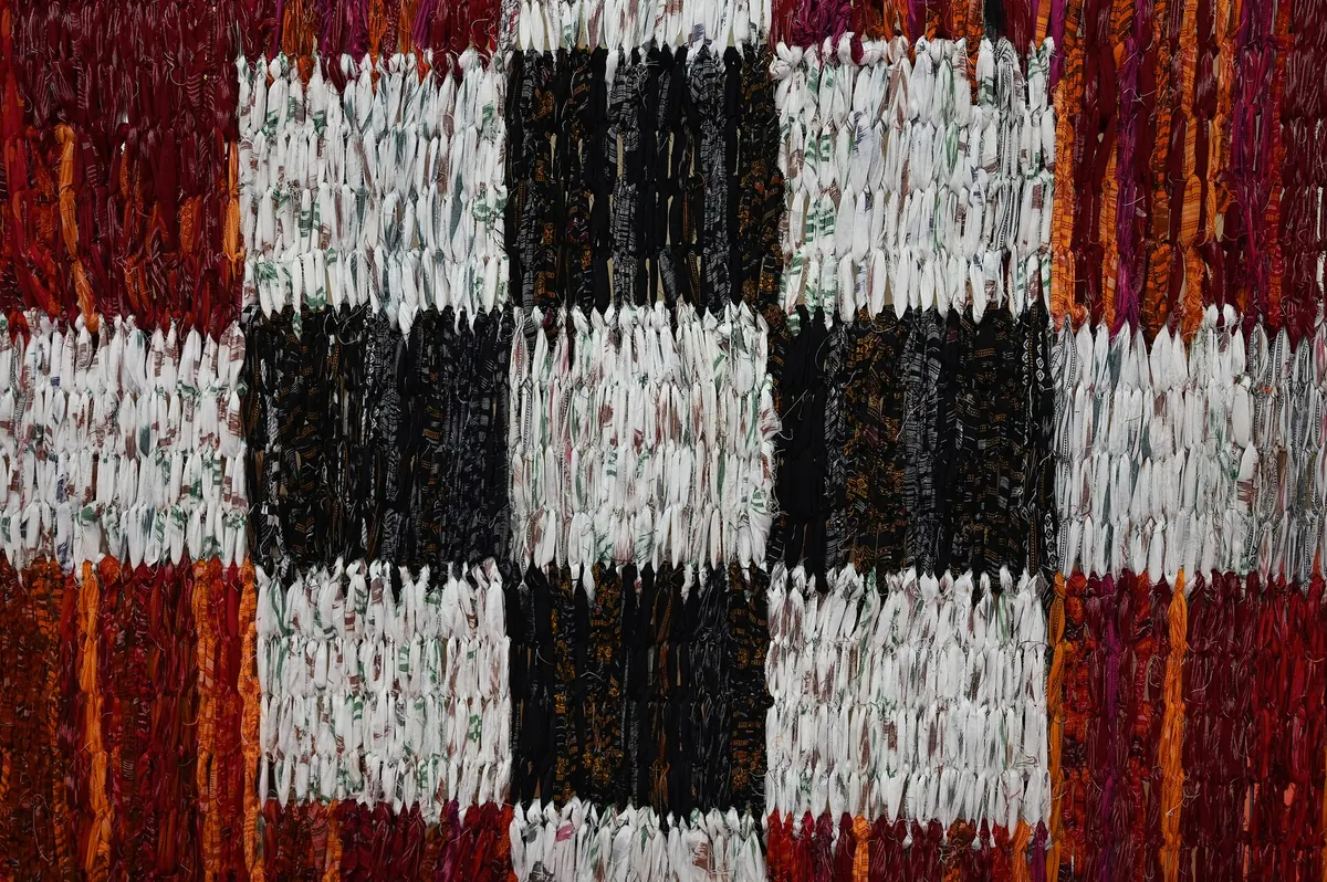 Close up of a pasapali saree: big squares of black and white, each one speckled with small tied motifs, edged in red.
