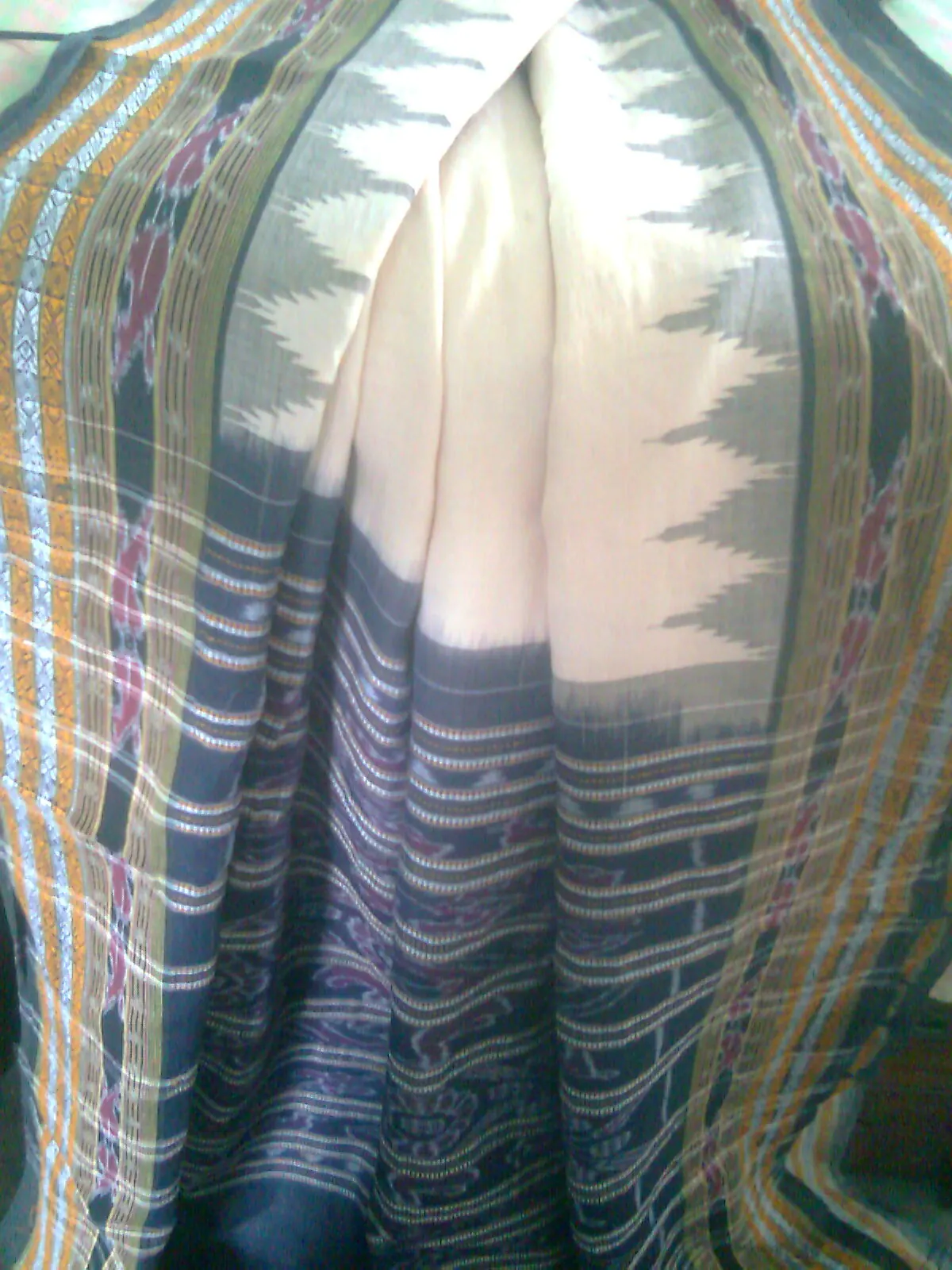A draped bandha saree in cream and dark green, its border a row of stepped white spires.